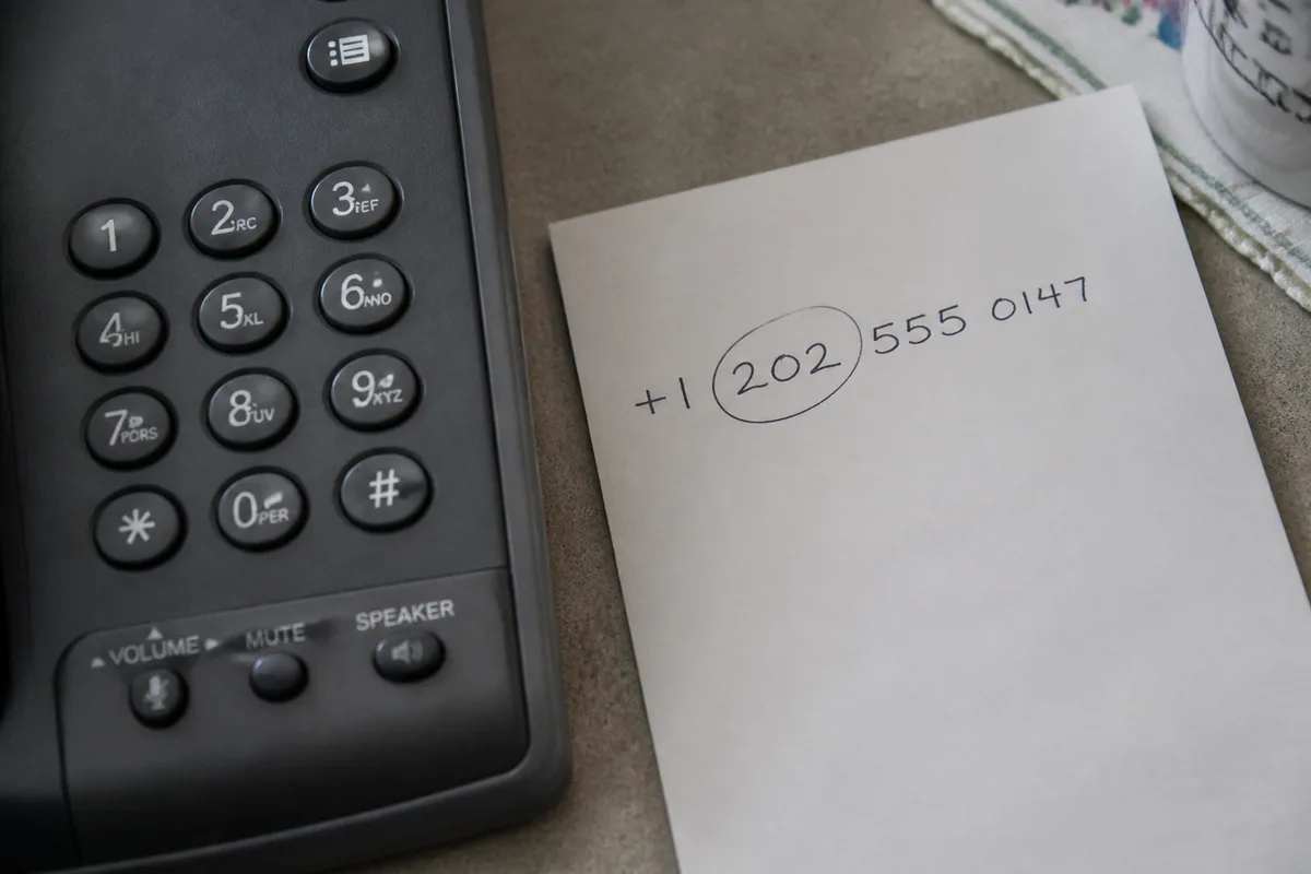 Physical US landline keypad beside a handwritten fictional phone number with the area code marked